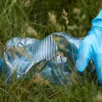 main gantée ramassant un déchet de bouteille plastique dans la nature